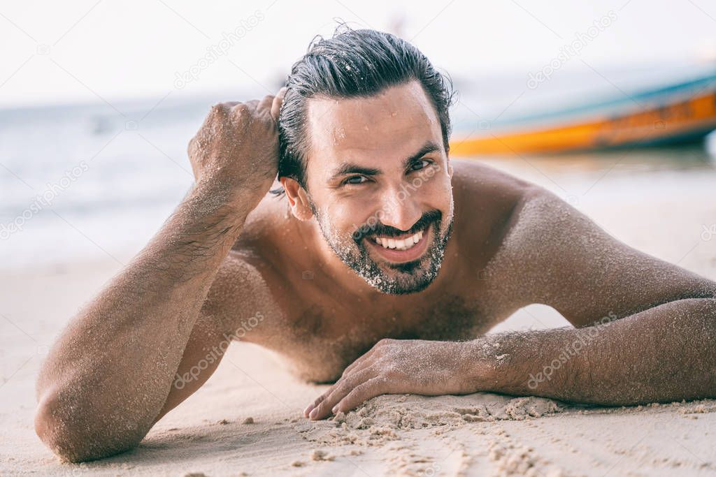 Young sexy stylish handsome latin man lies on tropical beach wit