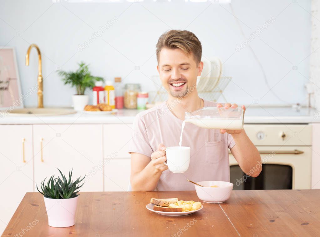Happy young blond man having breakfast in the kitchen with milk 