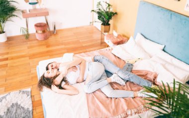 Yatak odasındaki mutlu genç çift eğleniyor, romantik vakit geçiriyor.