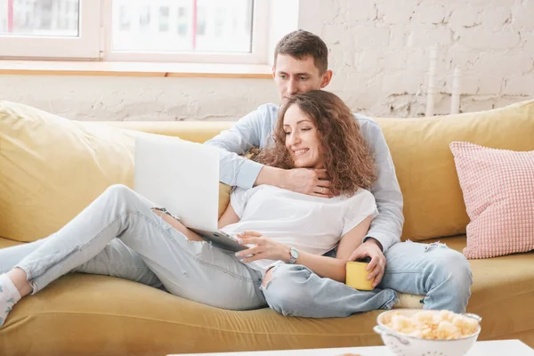 Молода щаслива пара лежить на жовтому дивані з ноутбуком в їх — стокове фото