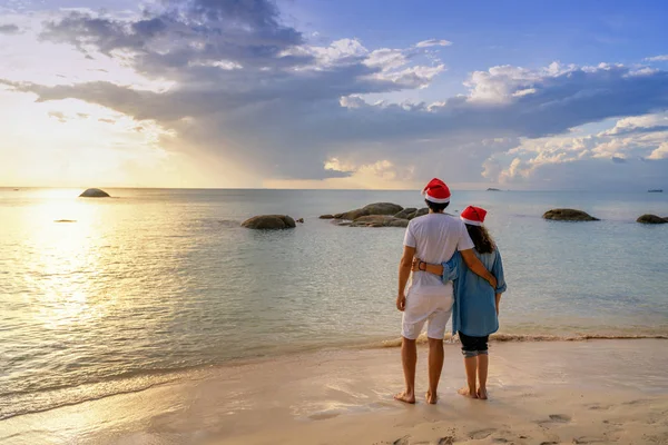 Молодая красивая пара в шляпах Санта-Клауса ходит вдоль берега — стоковое фото
