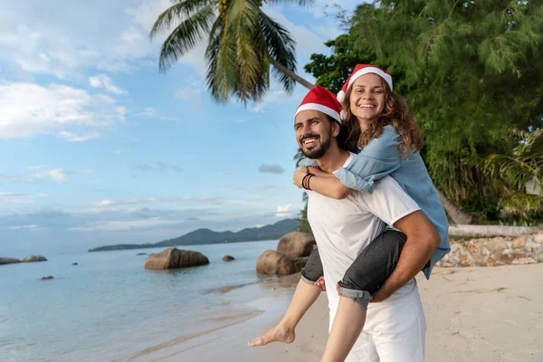 Jovem casal bonito em chapéus Papai Noel caminha ao longo da costa — Fotografia de Stock