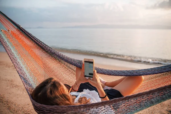 Девушка в гамаке со смартфоном, телефон в руках на солнце — стоковое фото