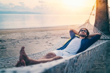 Young handsome Latin man in sunglasses relaxing in a hammock on 