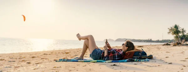 若い女性はビーチでスマートフォンに横たわっていた。リラクゼーション・コンプ — ストック写真