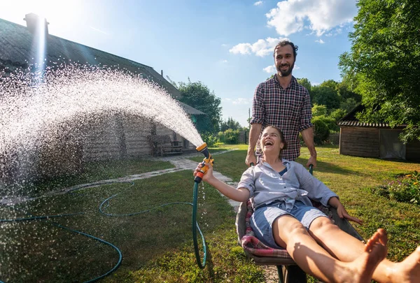 Unga lyckliga par vattning trädgård, en flicka med en slang i handen o — Stockfoto