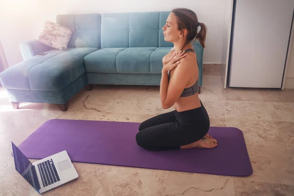 Lessons of meditation breathing and yoga at home, a woman is engaged in the living room in front of a laptop.