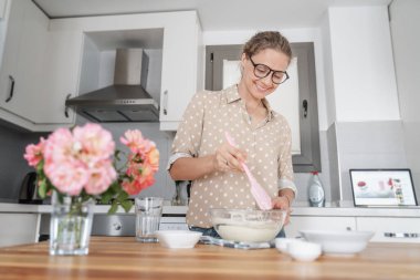 Mutfakta tatlı hazırlayan ve internette akıllı telefondan yemek yapan, evde yemek yapan hobileri ve eğlenceleri olan, mangırı spatulayla karıştıran genç bir kadın..