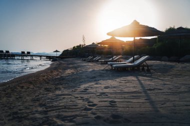 Deniz kenarında güneşli yatakları ve şemsiyeleri olan boş kumlu bir sahil. Yaz tatili konsepti.