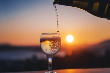 Beyaz şarap, gün batımında şehir manzaralı cam bir bardağa dökülüyor..