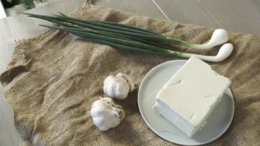 Büyük bir parça tereyağı, arka planda sarımsaklı ve yeşil soğanlı.