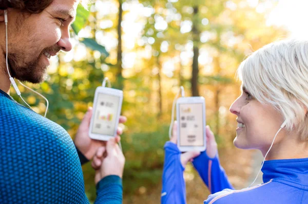 Runnen van paar met slimme telefoons en oortelefoons — Stockfoto