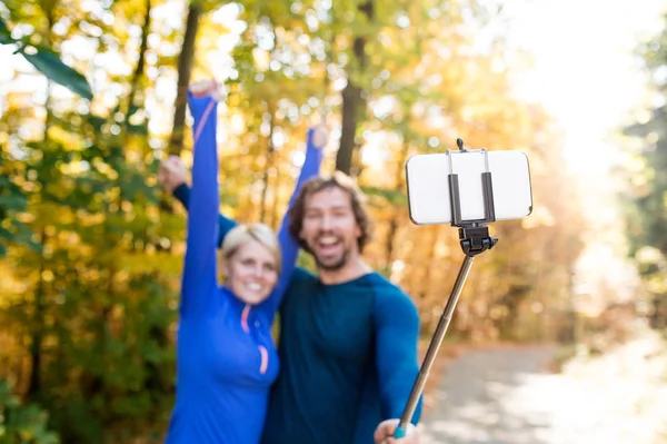 Beautiful runners in autumn forest taking selfie with smartphone — Stock Photo, Image