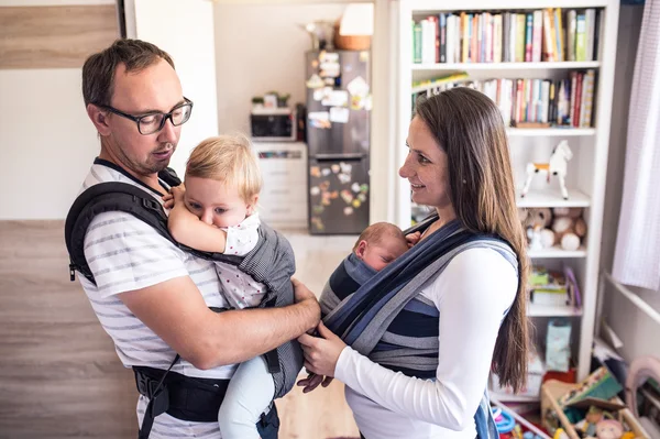 Padres jóvenes con niños en cabestrillo y portabebés — Foto de Stock