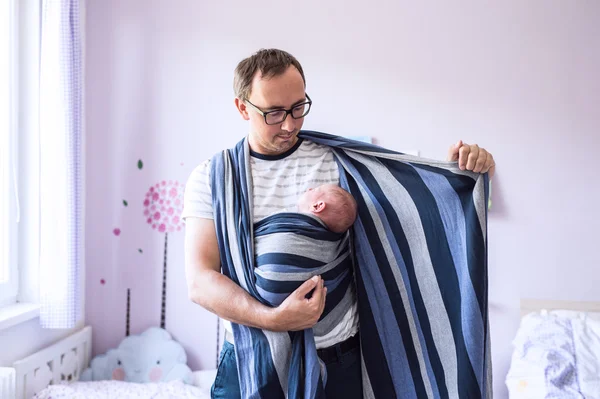 Молодой отец заворачивает своего новорожденного сына в стропу — стоковое фото