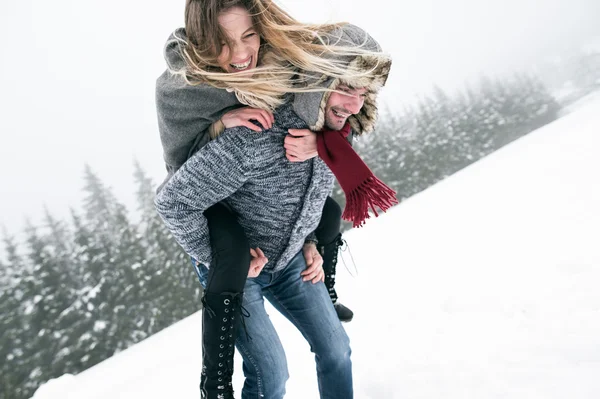 Man giving woman piggyback in winter — Stock Photo, Image