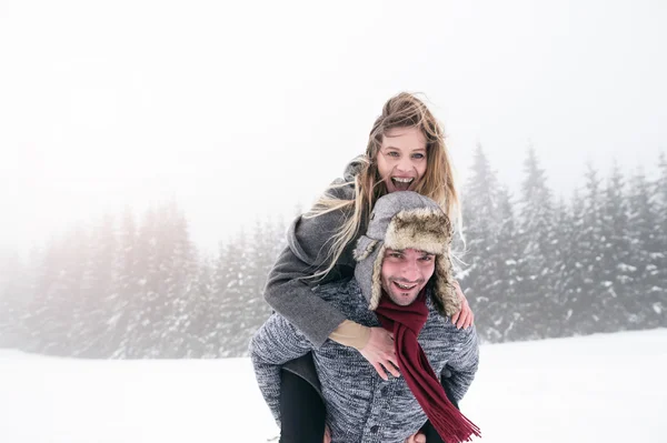 Man giving woman piggyback in winter — Stock Photo, Image