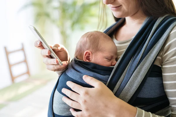 Ibu dengan anak di sling dan smartphone — Stok Foto