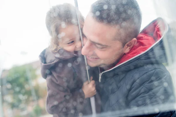Junger Vater hält Tochter unter dem durchsichtigen Regenschirm. — Stockfoto
