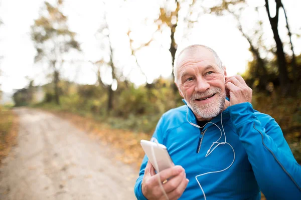 Senior löpare i naturen med smart telefon med hörlurar. — Stockfoto