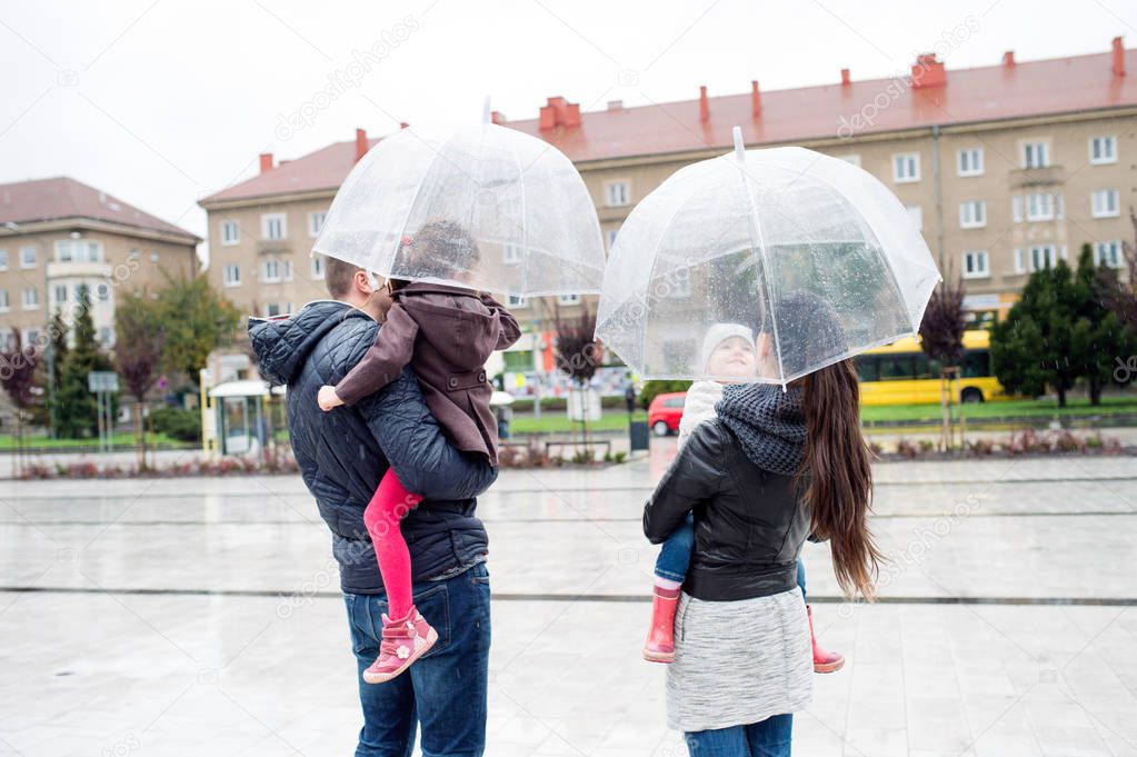 Young family with two daughters under the umbrellas, town