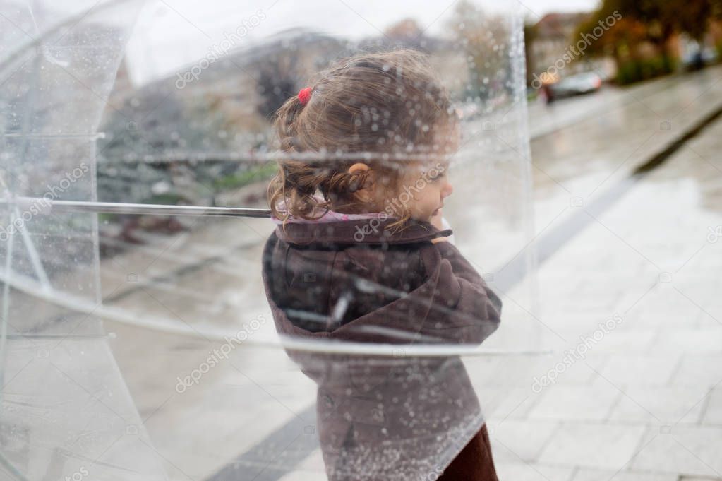 Little girl under the transparent umbrella outside, rainy day.