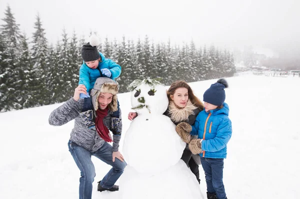Pais com seus filhos, brincando na neve, construindo boneco de neve . — Fotografia de Stock