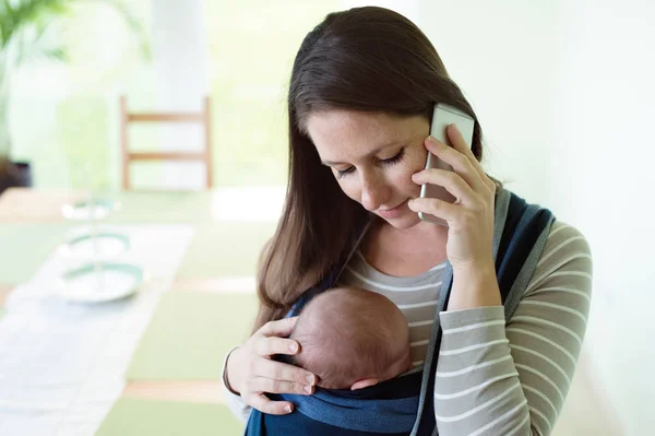 แม่ที่สวยงามกับลูกชายของเธอในสลิงและสมาร์ทโฟน — ภาพถ่ายสต็อก