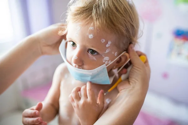 Little girl with chickenpox, mother giving her protective mask — Stock Photo, Image