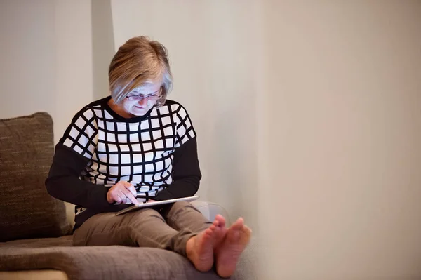 高级的女人坐在客厅的沙发上的平板电脑 — 图库照片