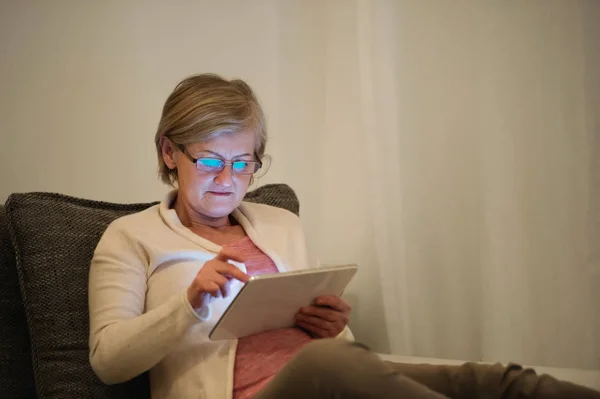 Mujer mayor con la tableta sentada en el sofá en la sala de estar — Foto de Stock