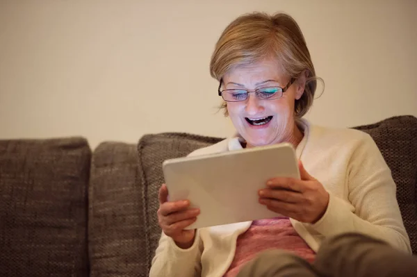Старша жінка з планшетом сидить на дивані у вітальні — стокове фото