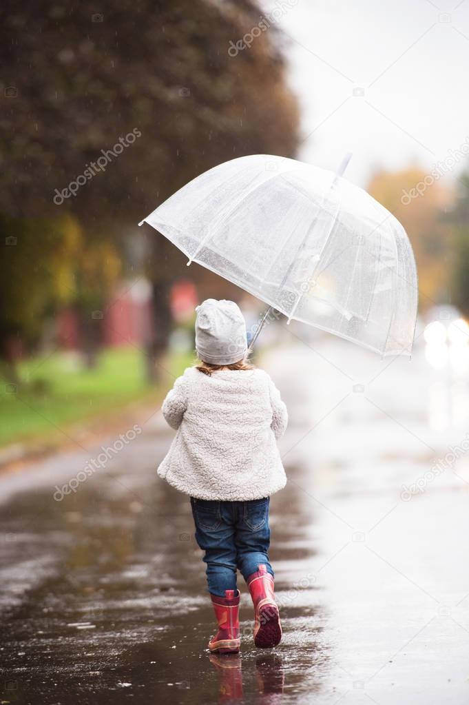 Little girl under the transparent umbrella outside, rainy day.