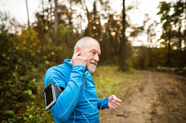 Seniorenläufer in der Natur mit Smartphone und Kopfhörer. — Stockfoto
