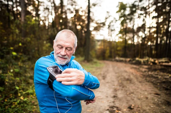 Corredor senior en la naturaleza con teléfono inteligente y auriculares . — Foto de Stock