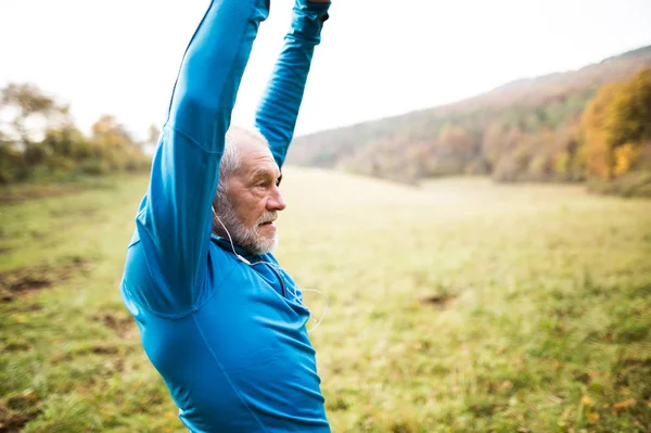 Senior runner with earphones doing stretching. Autumn nature.