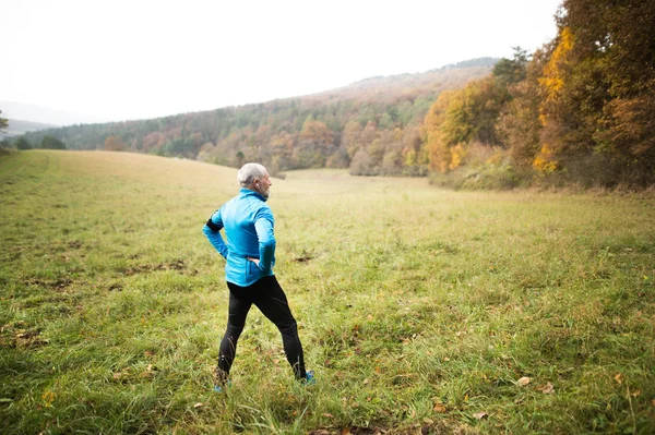 Senior-Läufer mit Kopfhörern beim Stretching. Herbstliche Natur. — Stockfoto