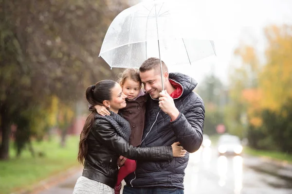 在遮阳伞下的女儿一家人漫步在雨天. — 图库照片