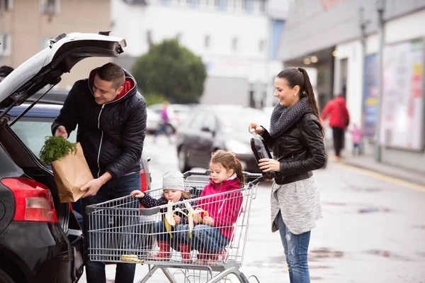 Padres empujando carrito de compras con comestibles y sus hijas —  Fotos de Stock