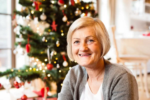 Senior woman in front of illuminated Christmas tree. — Stock Photo, Image