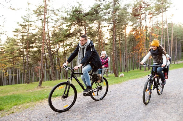年轻的家庭，在暖和的衣服，在秋天公园骑自行车 — 图库照片