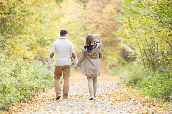 Beautiful young family on a walk in autumn forest.