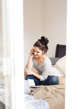 Telefon görüþmesi yatağın üstüne oturan bir bayan. Ev ofis.
