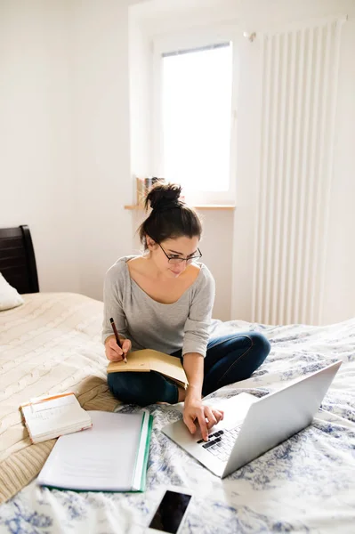 Schöne junge Frau sitzt auf dem Bett und arbeitet. Innenbehörde. — Stockfoto