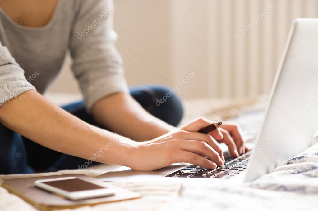 Unrecognizable young woman sitting on bed, working. Home office.