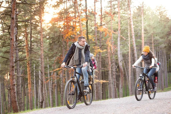 Familia joven en ropa de abrigo en bicicleta en el parque de otoño —  Fotos de Stock