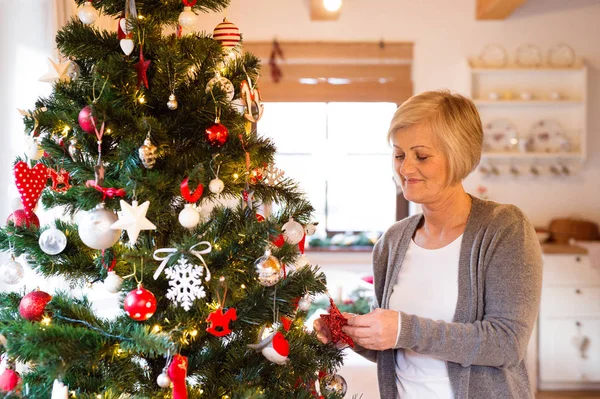 Senior woman at home decorating Christmas tree.