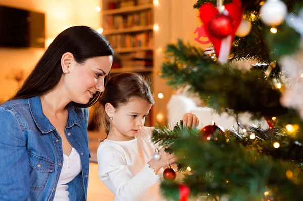 Junge Mutter mit Tochter schmückt gemeinsam Weihnachtsbaum. — Stockfoto