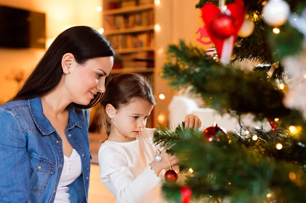 Ung mor med daugter dekorera julgran tillsammans. — Stockfoto