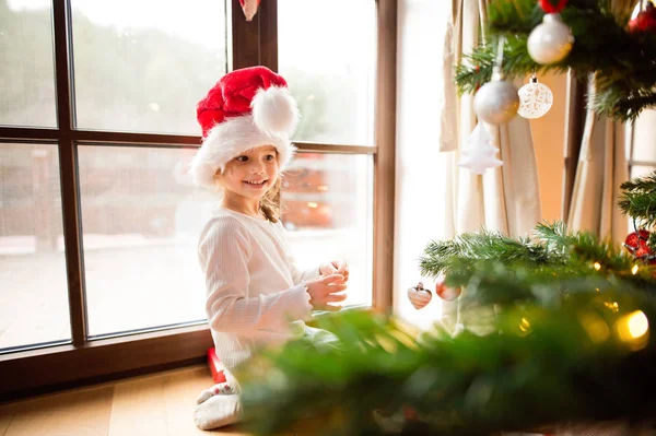 Little girl wearing red hat decorating Christmas tree.